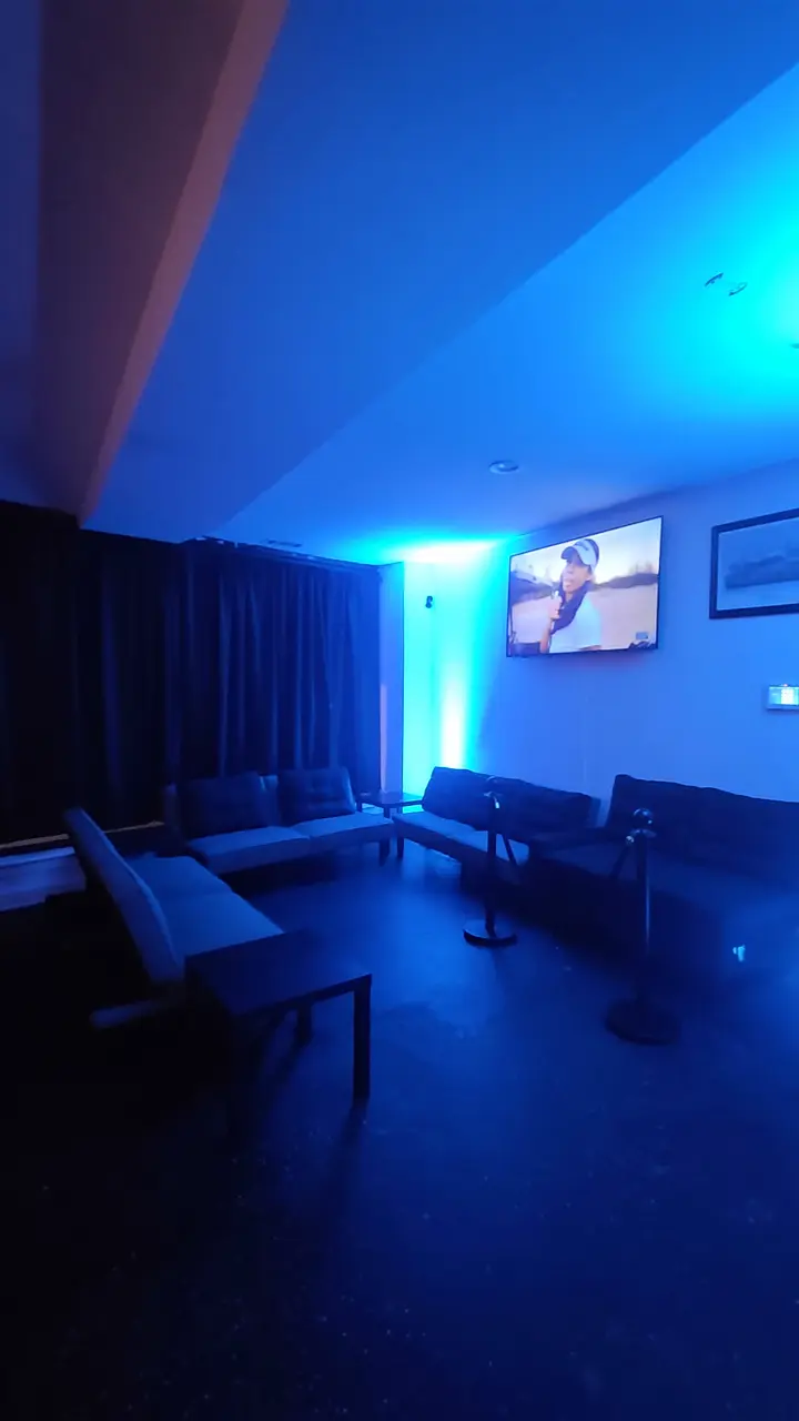The corner lounge glowing cyan, with velvet rope and a screen on the far wall.